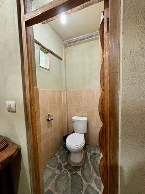 A small bathroom with a toilet, a shower area, and a wooden door frame. - Salkantay Hostel Chaullay (Santa Teresa)
