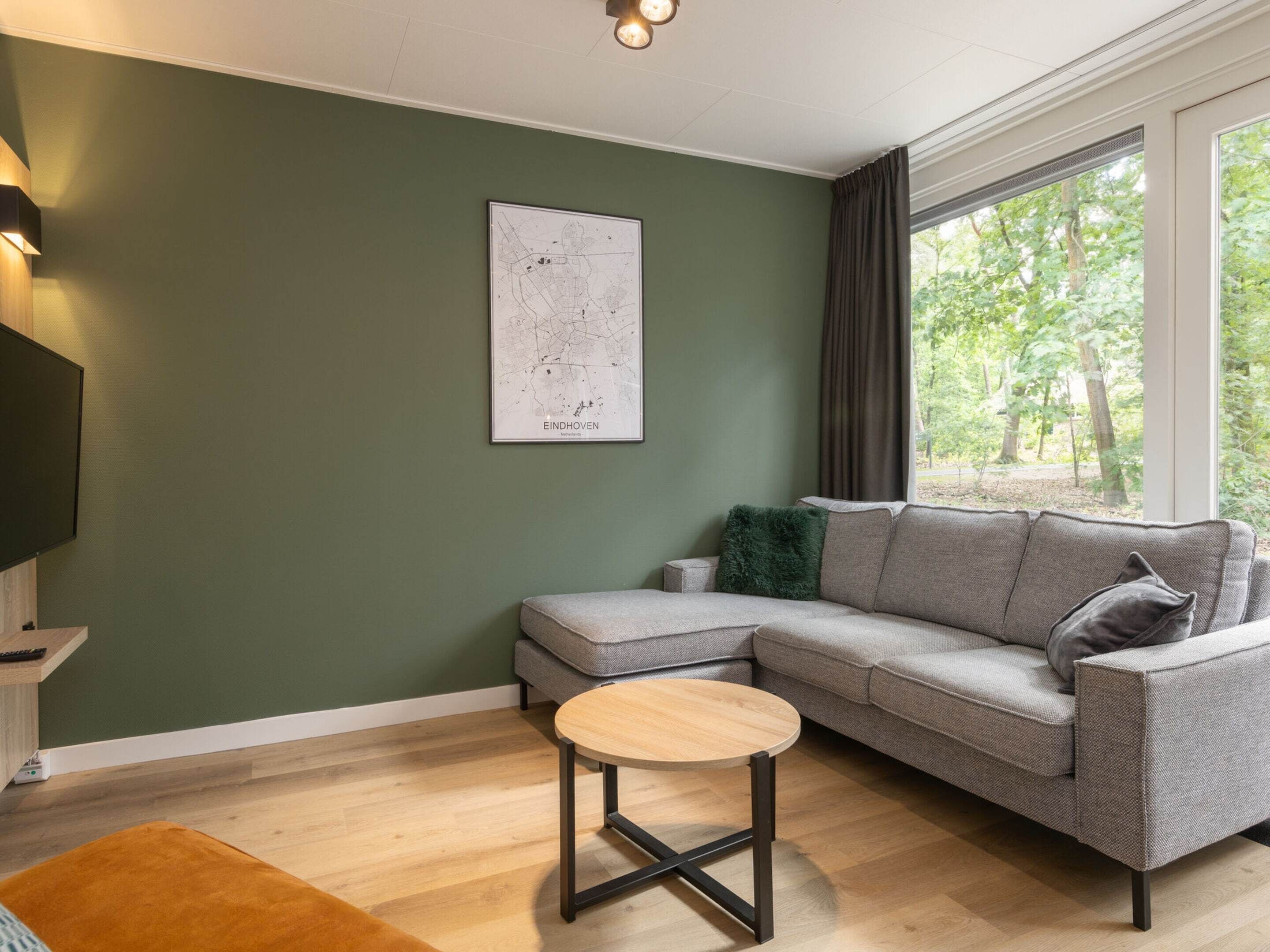 A modern living room with a sectional sofa, a round coffee table, and a map of Eindhoven on the wall.