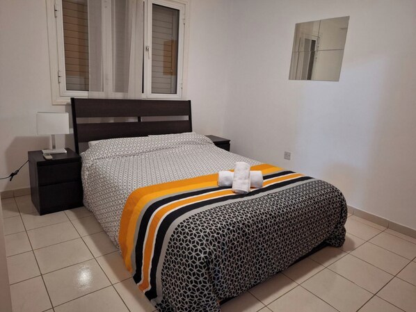 A neatly arranged bedroom with a bed, a nightstand, a lamp, and a window with blinds. - City Sunshine Strovolos, Nicosia (Strovolos)