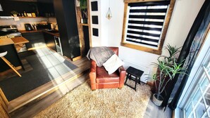 Un espacio habitable moderno con una zona de estar acogedora, una cocina y un amplio ventanal con persianas.