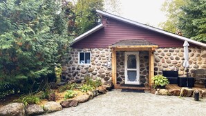 Un edificio de piedra con puerta de madera, una ventana pequeña y un porche con mobiliario exterior.
