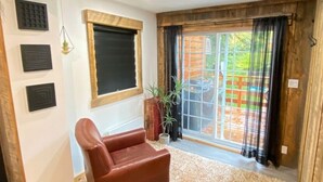Una habitación con techo de madera, un sillón de cuero marrón, una ventana con persiana negra y un ventanal corredero que da al exterior.