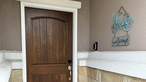 Eine Holztür mit weißem Rahmen, eine Fußmatte, ein kleiner Blumentopf und ein an der Wand befestigtes Schild mit Fahrradzeichen.