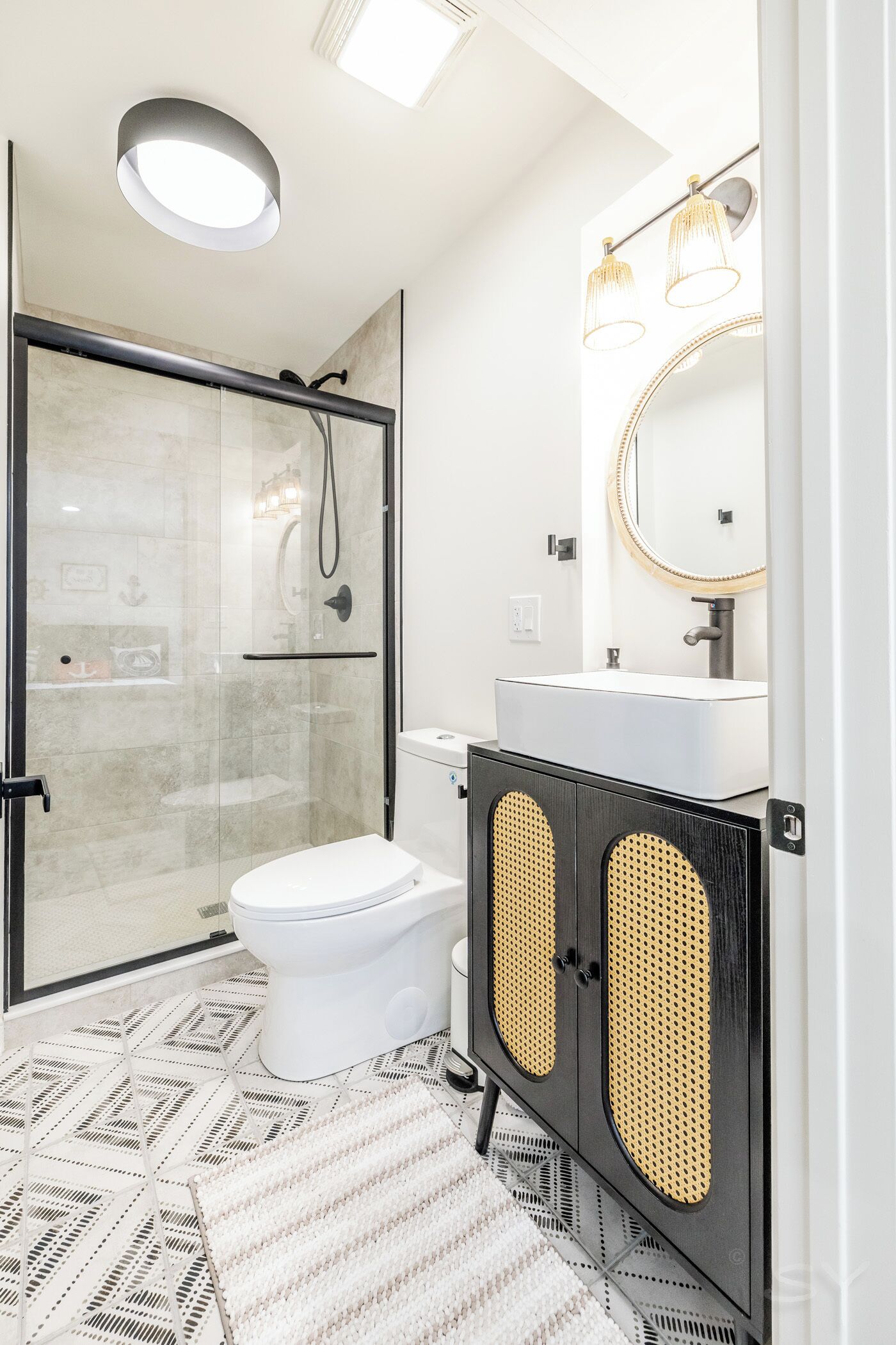 Ein modernes Badezimmer mit einer gläsernen Duschkabine, einer weißen Toilette, einem Waschbecken mit Spiegel und einem schwarzen Korpus mit Flechtpaneelen.