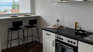 A compact kitchen with white cabinets, a black countertop, and a view of the sea through a window. - Apartment Emilio - Small apartment with great lake and alpine views (Überlingen)