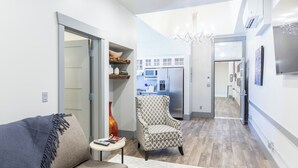 A modern living room with a sofa, armchair, and a small table with books and a vase. A kitchen is visible in the background with a refrigerator and microwave. - Bell Sister Flats (Roseburg)