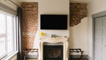 Een kamer met een bakstenen muur, een open haard met een witte boordplank, een flatscreen televisie erboven en een deur aan de rechterkant.