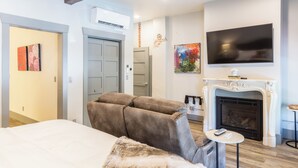 A modern hotel room with a large bed, a sofa, a fireplace, and a TV mounted on the wall. - Bell Sister Flats (Roseburg)