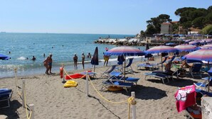 A beach with umbrellas, lounge chairs, and people swimming. - Cinque Terre Campsite Chalet 328 Near the sea (Ameglia)