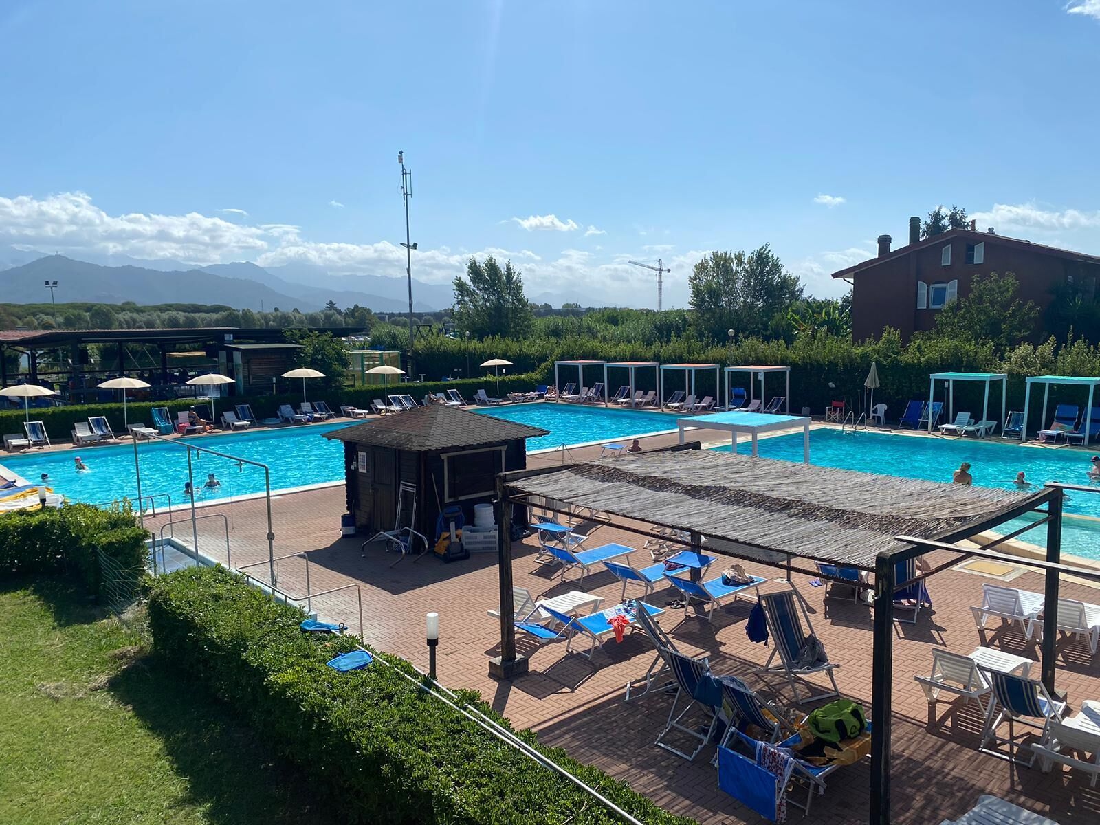 A swimming pool area with multiple pools, lounge chairs, umbrellas, and a small hut.