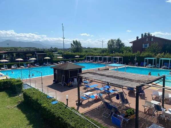 Un área de piscina con varias piscinas, sillas de descanso, sombrillas y una pequeña cabaña.