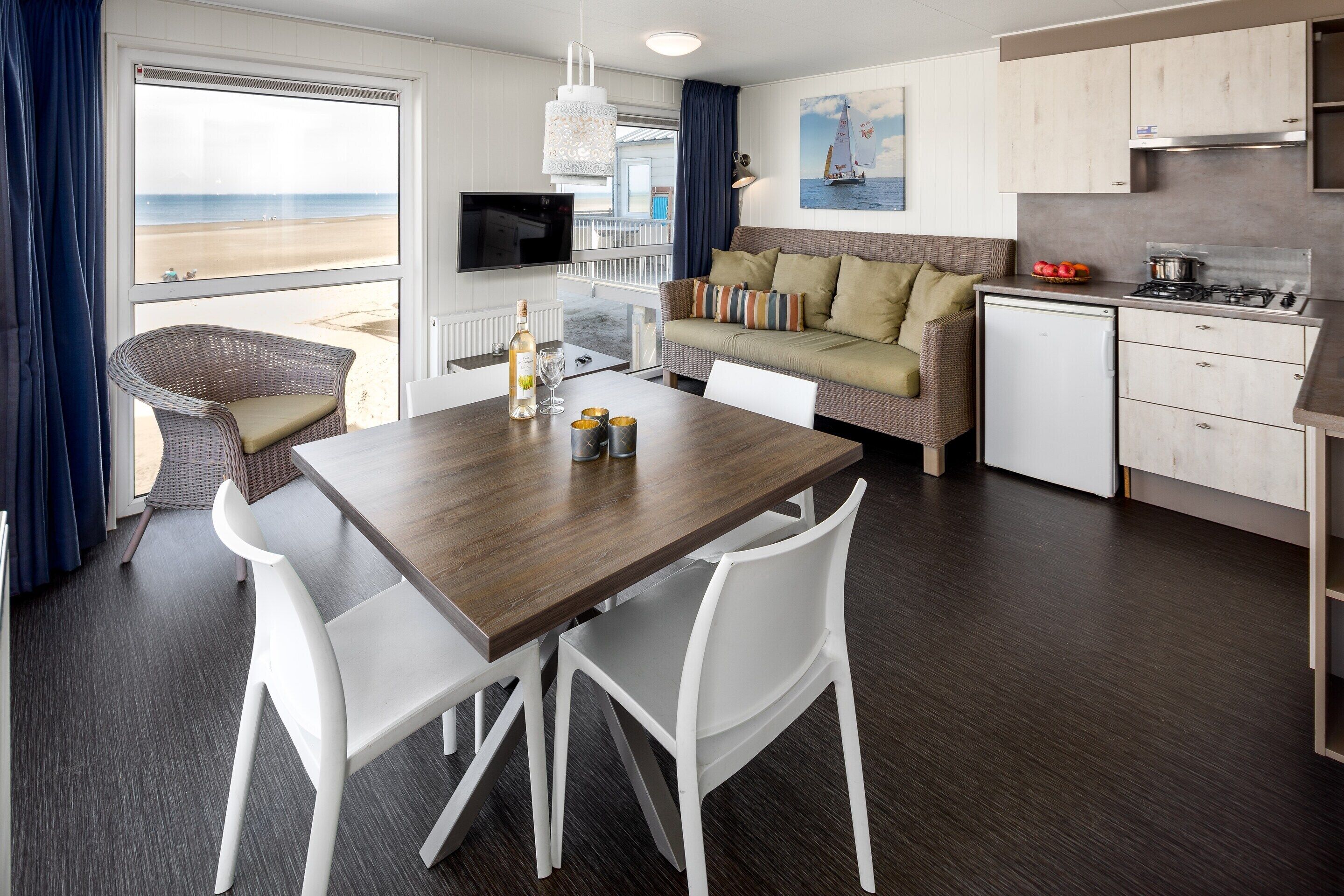 A compact living space with a dining area, kitchenette, and a large window overlooking a beach.
