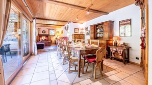Een eetgedeelte met een lange houten tafel, stoelen en een keuken met kastjes en een fornuis.