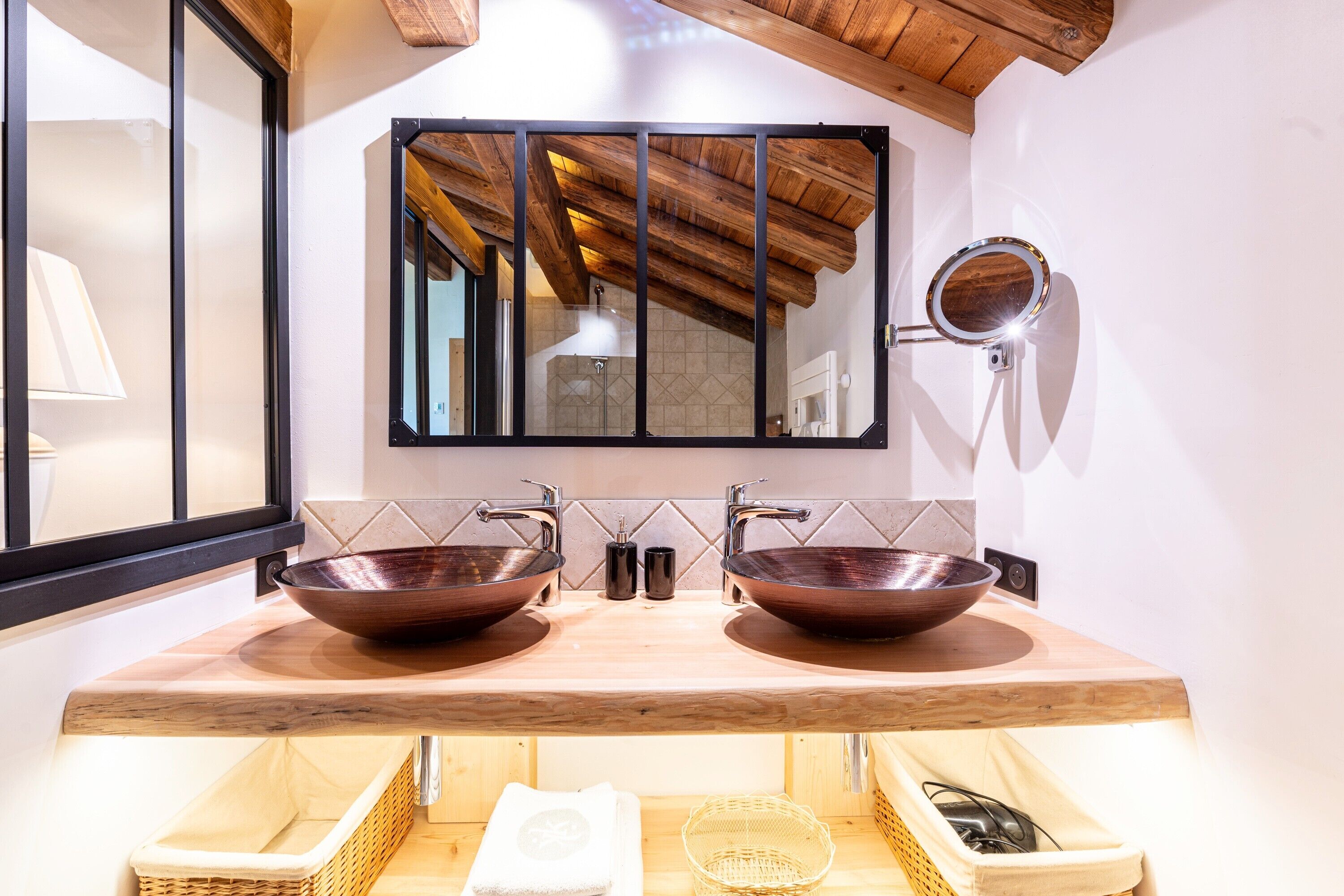 Une salle de bain avec deux vasques en cuivre, un meuble-lavabo en bois, un grand miroir et un porte-serviettes.