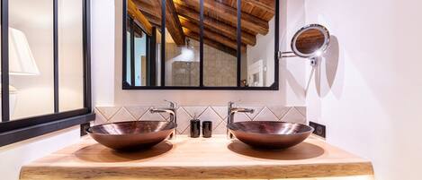 Une salle de bain avec deux vasques en cuivre, un meuble-lavabo en bois, un grand miroir et un porte-serviettes.