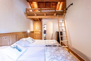 A room with two beds, wooden headboard, a loft bed, a ladder, and a door leading to another room. - Chalet 'Le Courti' with Mountain View, Private Terrace and Wi-Fi (Sainte-Foy-Tarentaise)