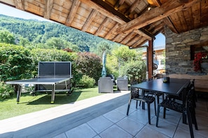 An outdoor patio with a ping pong table, seating, and a stone wall.