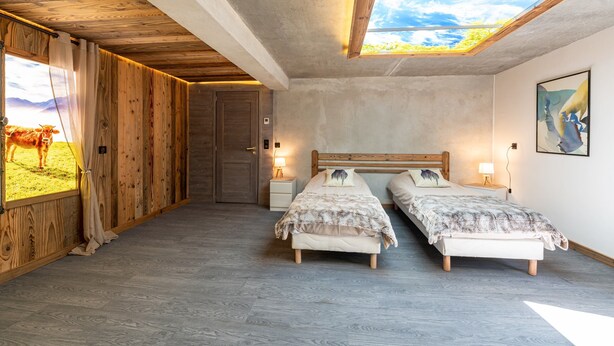 Een slaapkamer met twee bedden, een dakraam, houten wanden en uitzicht op een koe door het raam.