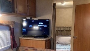 Un intérieur de camping-car compact comprenant un coin cuisine, un téléviseur, une petite table à manger et un espace nuit.