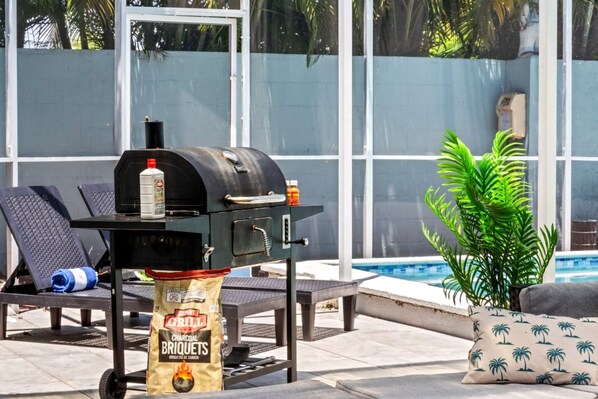 An outdoor grill with charcoal briquets, a bottle of barbecue sauce, and a bottle of water on a table.