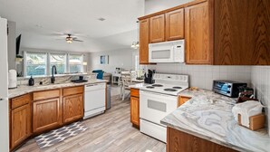 A modern kitchen with wooden cabinets, white appliances, and a marble countertop. - Extended Stay Fun Outdoor Games Gym BBQ and Dining (Lewisville)