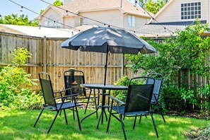 Une terrasse avec une table et quatre chaises, un parasol et une clôture en bois en arrière-plan.