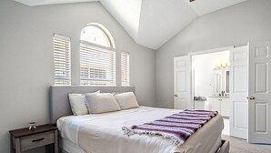 A bedroom with a large bed, a nightstand, a window with blinds, and a door to a bathroom. - Extended Stay Fun Outdoor Games Gym BBQ and Dining (Lewisville)