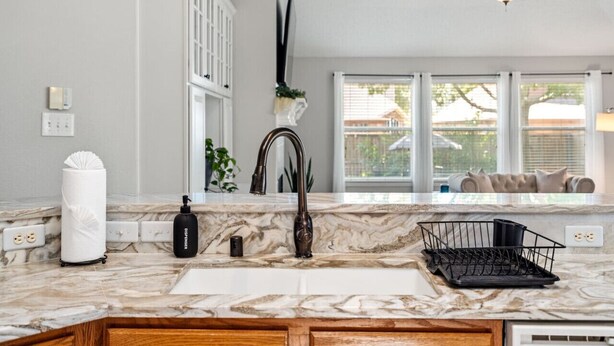 A kitchen with a marble countertop, a modern faucet, and a ceiling fan. - Extended Stay Fun Outdoor Games Gym BBQ and Dining (Lewisville)
