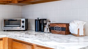 A kitchen with wooden cabinets, a toaster, a coffee maker, and a box labeled "Coffee Bar Premium Quality". - Extended Stay Fun Outdoor Games Gym BBQ and Dining (Lewisville)