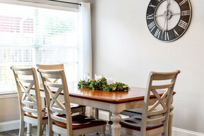 Un coin repas avec une table en bois, quatre chaises et une horloge fixée au mur.