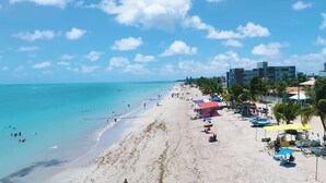 Een strand met helder turquoise water, een zandstrand en een rij gebouwen met palmbomen.