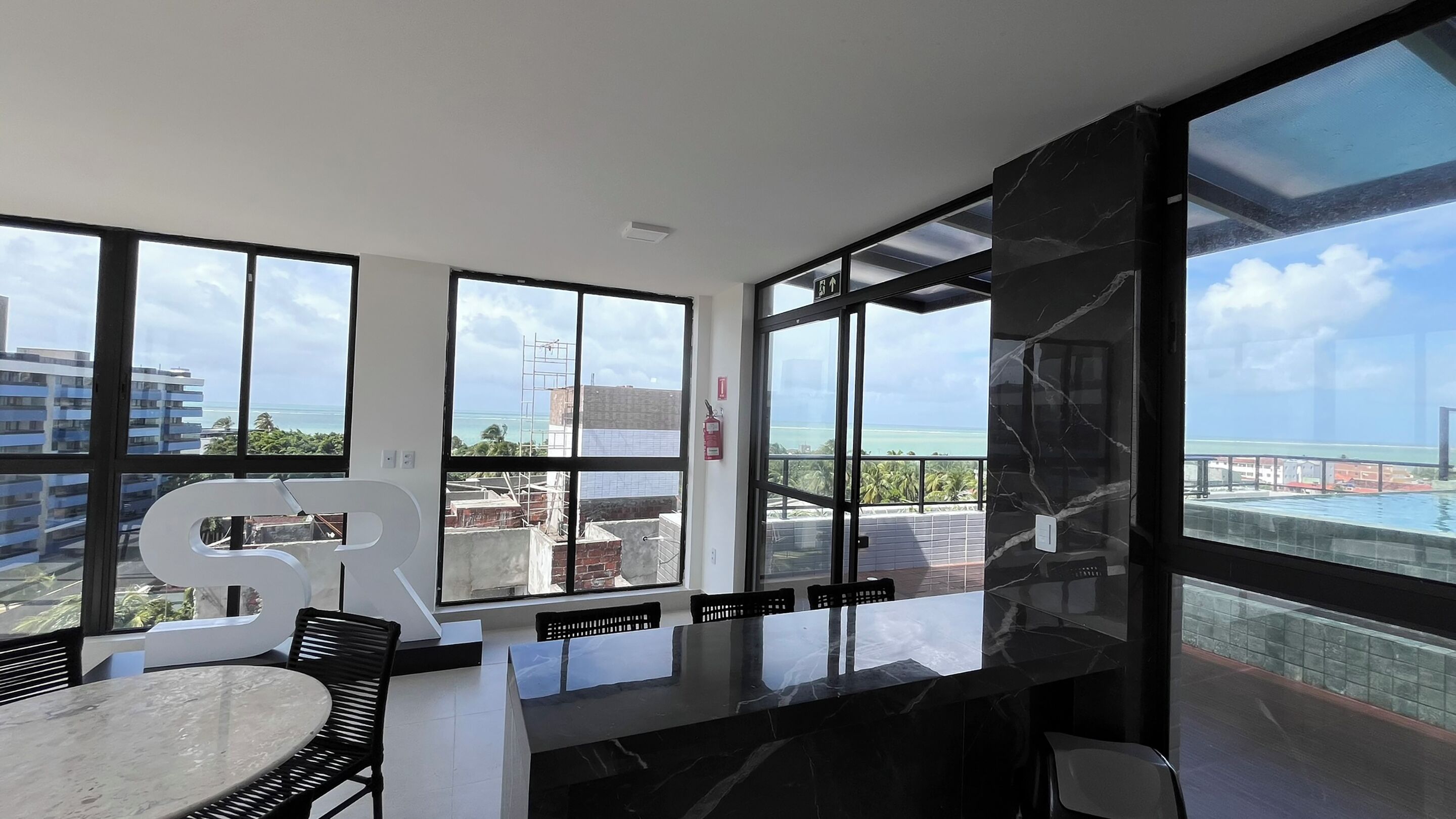 Une chambre moderne dotée de grandes fenêtres, d’une table en marbre et offrant une vue sur la mer et les bâtiments.