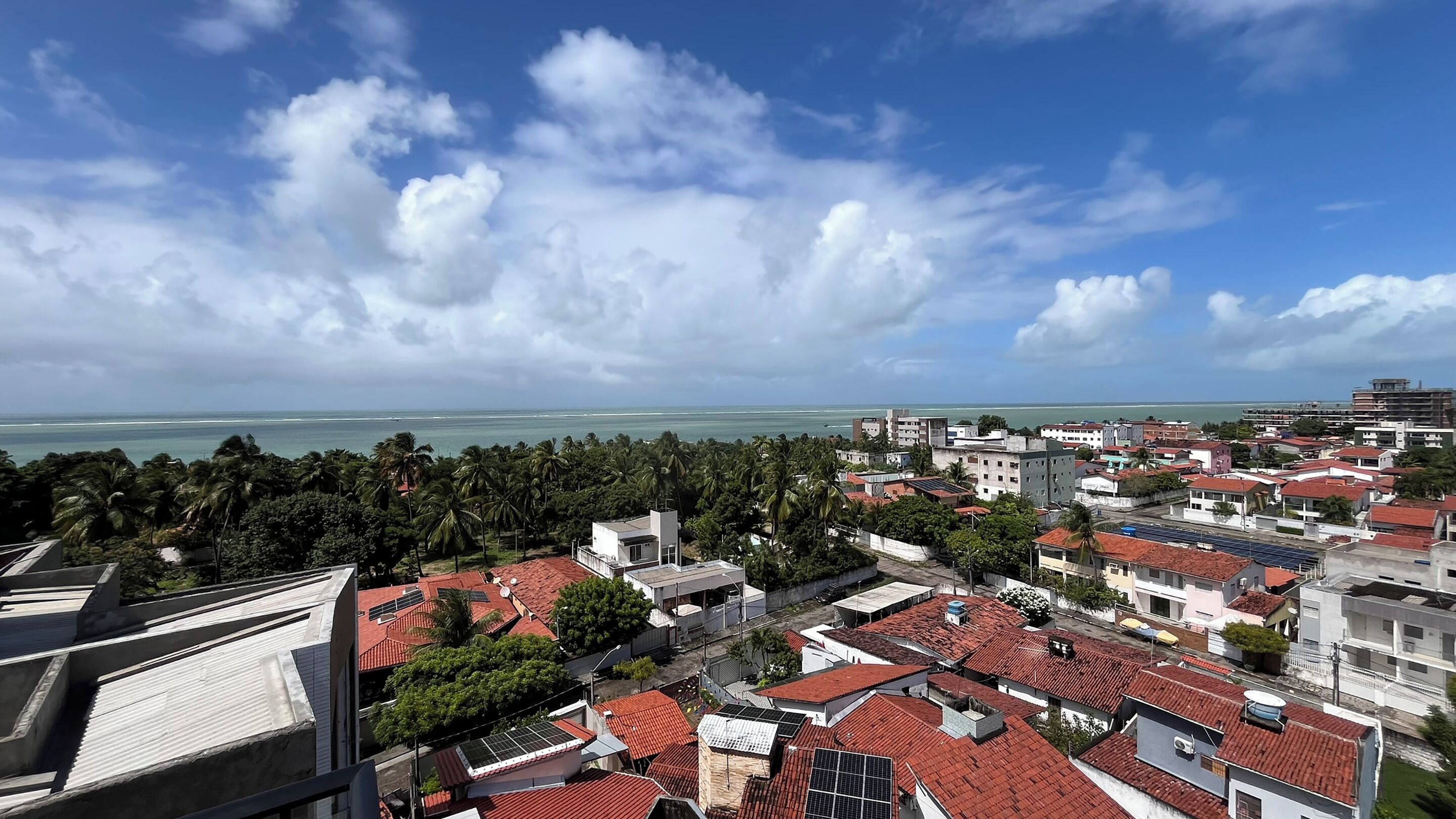 Zona residencial costera con tejados rojos, paneles solares y vista al mar.