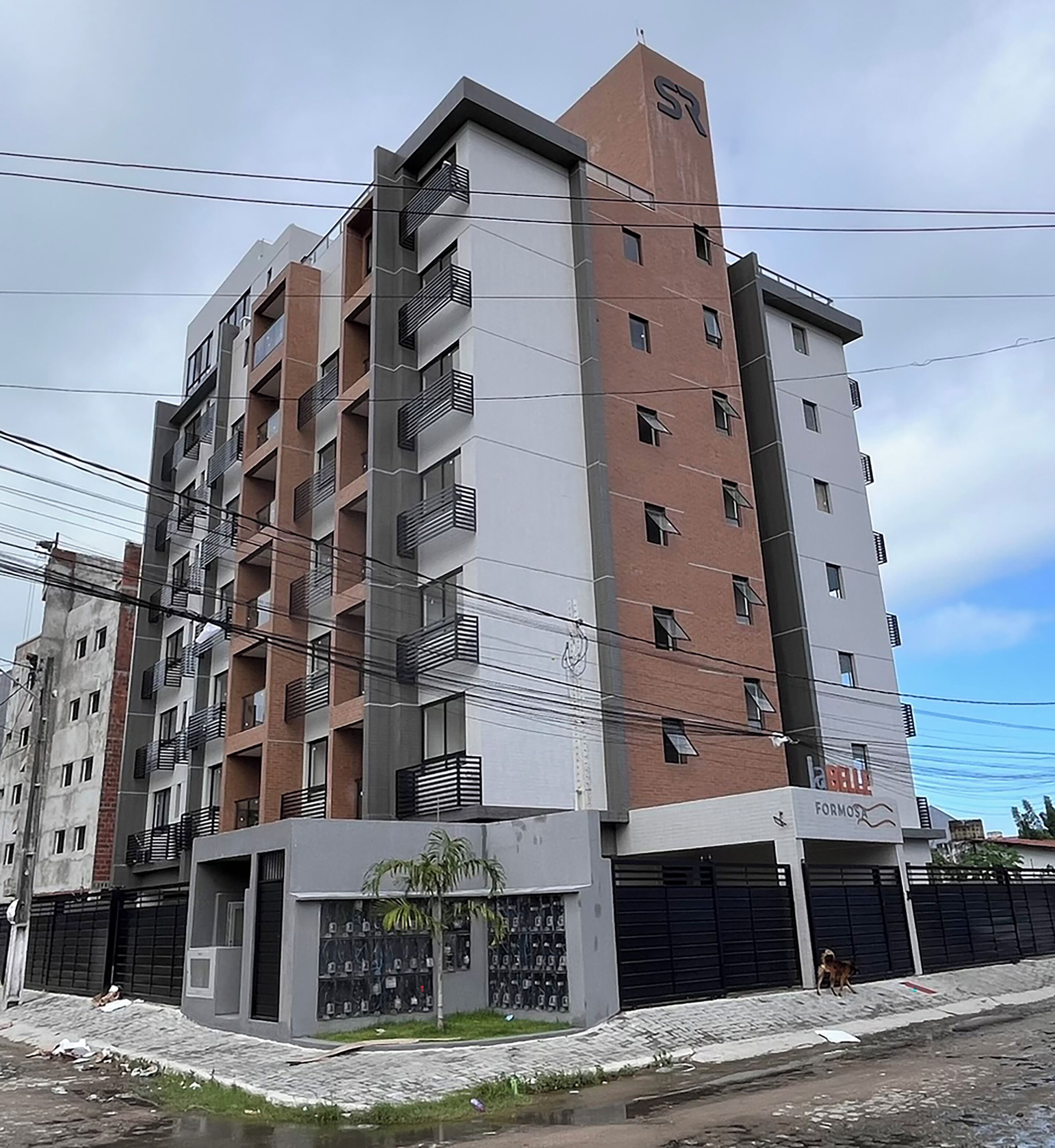 A multi-story residential building with balconies, a gated entrance, and a storefront with a sign.