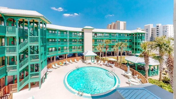 Un hotel con piscina central rodeada de sillones de descanso y un edificio de varios pisos con balcones.
