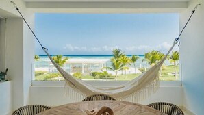 A hammock chair in a room with a view of the beach and palm trees. - Amazing ocean views apartment with private beach in Cap Cana (CAP CANA)