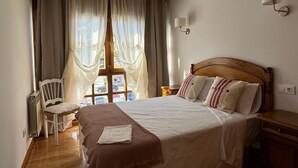 A bedroom with a wooden bed, a chair, a window with sheer curtains, and a wall-mounted lamp. - Apartamento Dúplex Aravedes en Potes (Potes)
