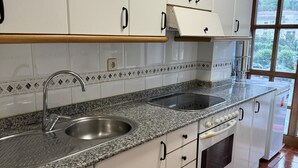 A kitchen with white cabinets, a granite countertop, a stainless steel sink, and a built-in oven. - Apartamento Dúplex Aravedes en Potes (Potes)