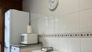 A compact kitchen with a refrigerator, microwave, washing machine, and a small table with a chair. - Apartamento Dúplex Aravedes en Potes (Potes)