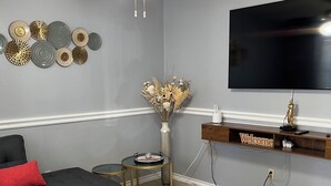 Una sala de estar con un sofá seccional negro, una mesa de centro redonda, un jarrón decorativo, un televisor de pantalla plana y un ventilador de techo.