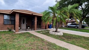 Una casa de ladrillo de un piso con porche delantero, una palmera y un camino de entrada con portón.