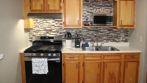 Cocina compacta con armarios de madera, estufa de acero inoxidable, microondas y salpicadero de azulejos.
