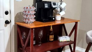 Una mesa de centro de madera con una cafetera, una pila de tazas y un porta vasos para vino.
