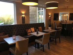 A cozy cafe with a wooden bench seating area, tables, and pendant lighting.