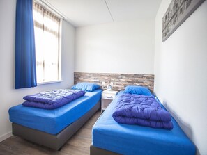 A bedroom with two single beds, a wooden headboard, a nightstand, and a window with curtains.