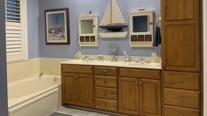 Un baño con lavamanos doble, armarios de madera, bañera e imagen enmarcada en la pared.