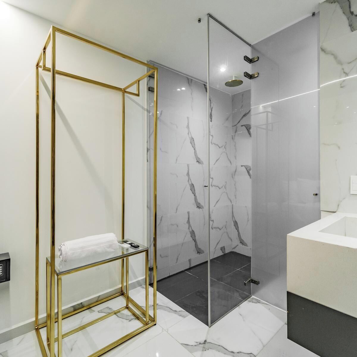 Een moderne badkamer met een glazen douchecabine, marmeren tegels en een gouden spiegelomkast.