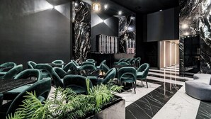 A modern lounge area with plush green chairs, marble walls, and a central plant display. - 444 jds (Medellín)