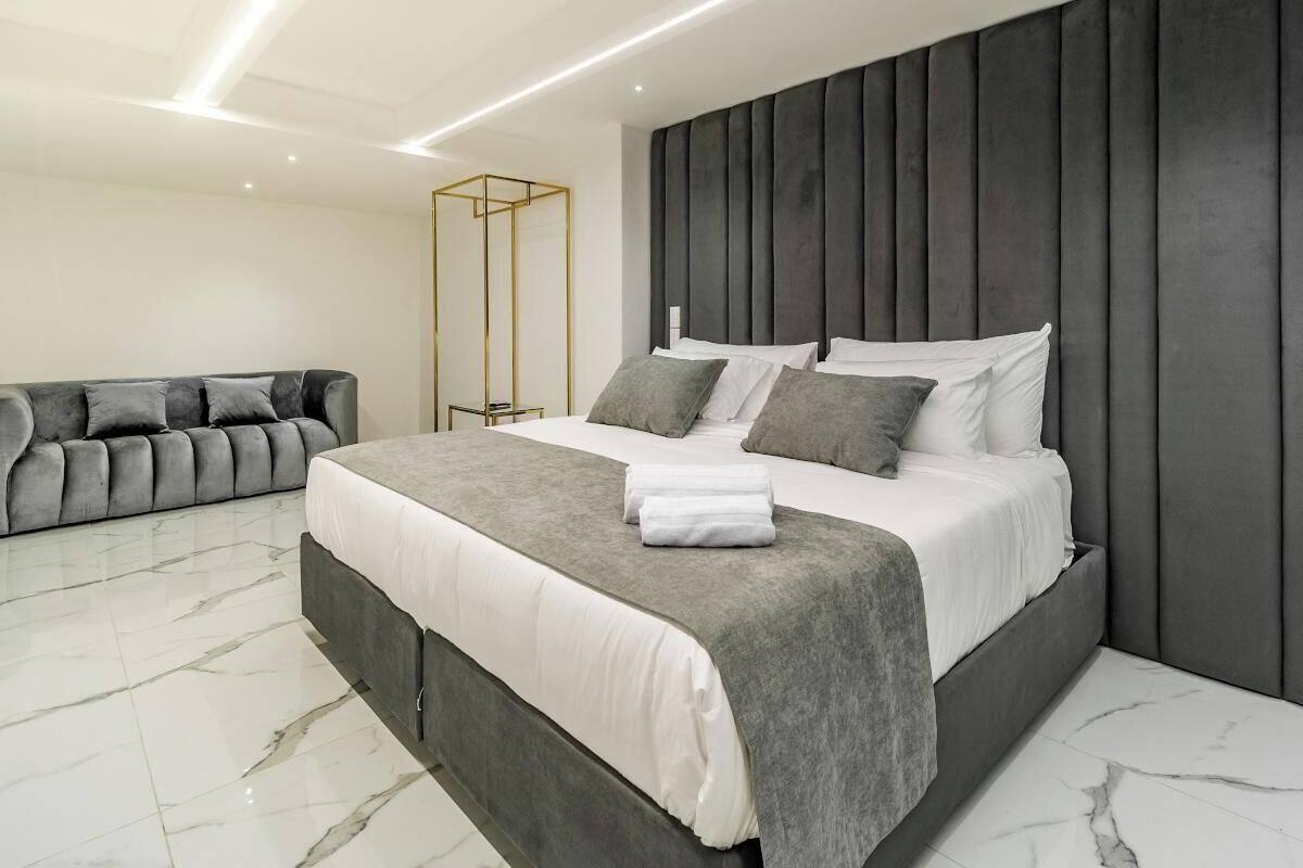 Un dormitorio moderno con una cama grande, un sofá gris y un suelo de mármol.