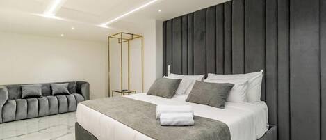 A modern bedroom with a large bed, a grey sofa, and a marble floor.